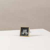 Mini fotolijstje van goud metaal en glas, met daarin een zwartwit foto van 2 kleine kindjes