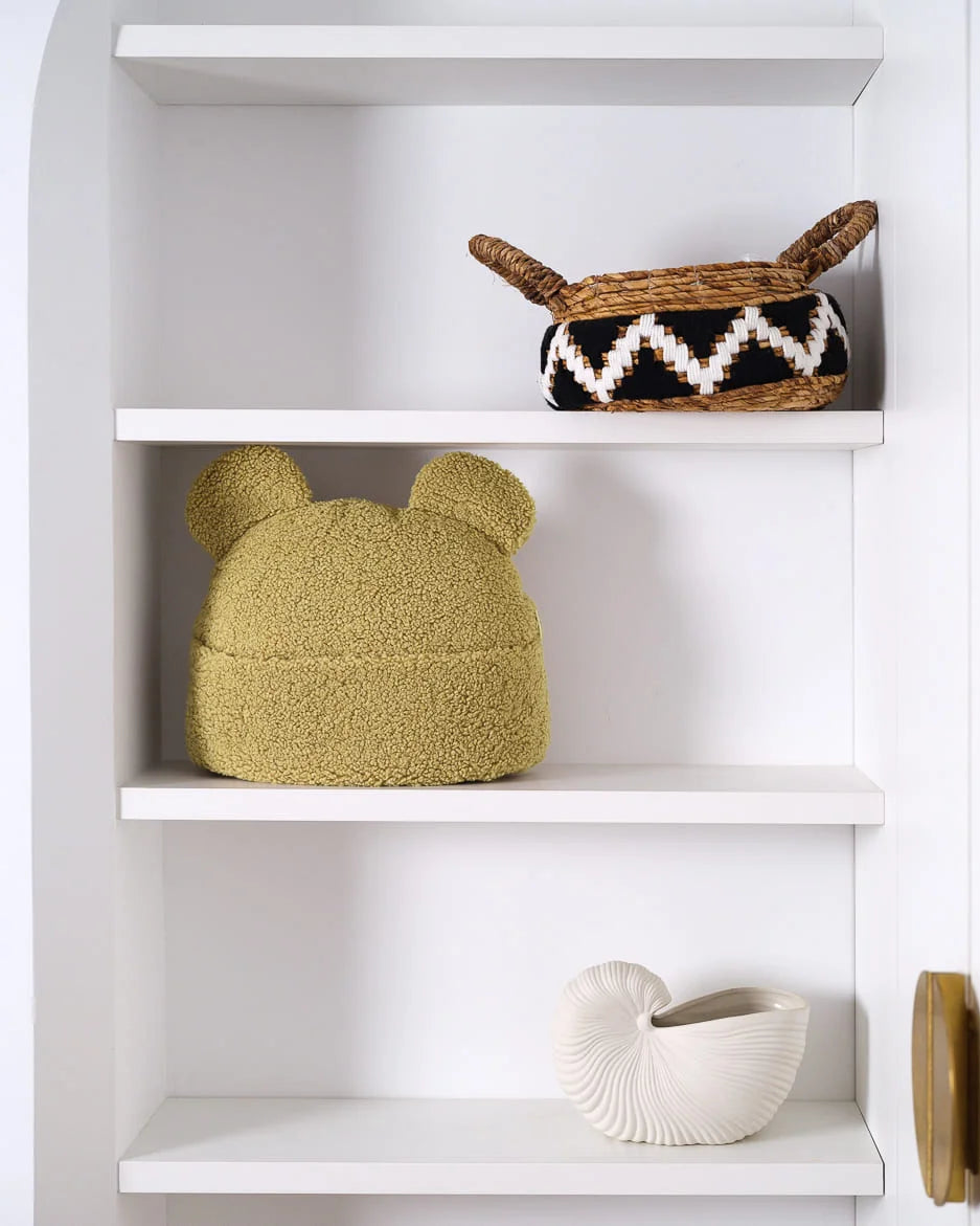 Het Wigiwama beerkussen in naturel zachtgroene matcha staat speels op een witte plank – een stijlvolle én functionele accessoire voor kinderkamers met een natuurlijke uitstraling.
