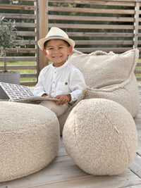 Het Wigiwama teddy kussen in biscuit kleur als speels accessoire in een zonnige buitenruimte. Ideaal voor lezen, relaxen en buitenplezier. Gecombineerd met een teddy poef en zitzak in dezelfde kleur en uit dezelfde serie.