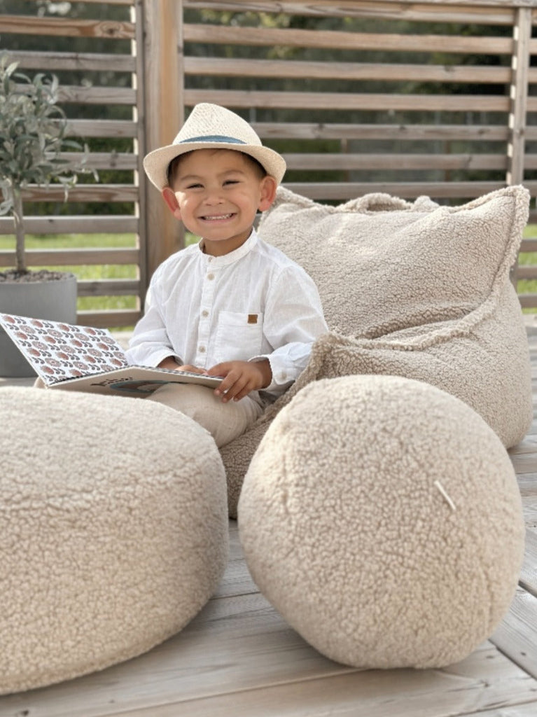 Het Wigiwama teddy kussen in biscuit kleur als speels accessoire in een zonnige buitenruimte. Ideaal voor lezen, relaxen en buitenplezier. Gecombineerd met een teddy poef en zitzak in dezelfde kleur en uit dezelfde serie.