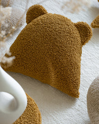 Dichtbij gefotografeerd zie je de rijke textuur van de OEKO-TEX® teddystof in de kleur maple. Dit zachte kussen in berenvorm is niet alleen een leuk accessoire, maar biedt ook comfort en karakter aan elke kinderslaapkamer.