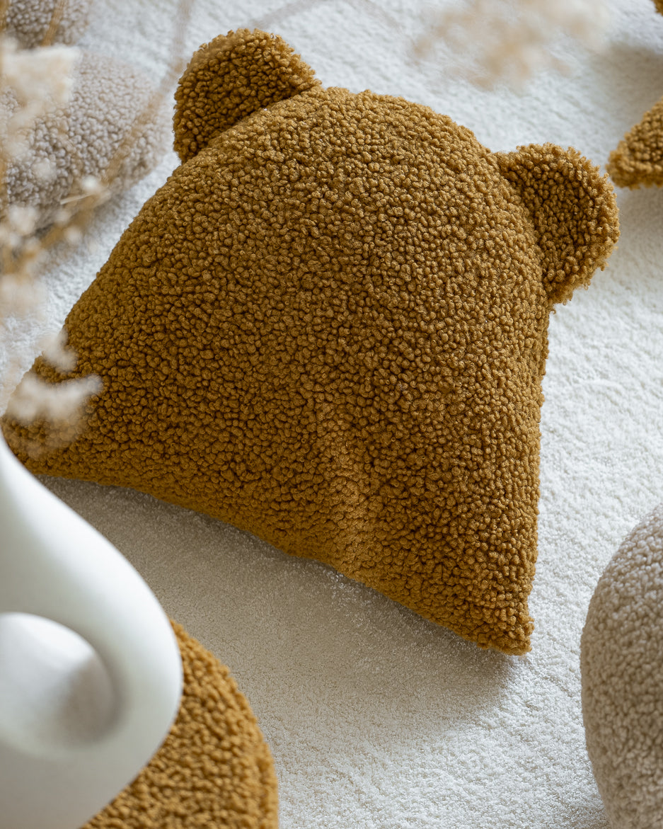 Dichtbij gefotografeerd zie je de rijke textuur van de OEKO-TEX® teddystof in de kleur maple. Dit zachte kussen in berenvorm is niet alleen een leuk accessoire, maar biedt ook comfort en karakter aan elke kinderslaapkamer.