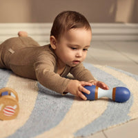 Baby speelt met de houten maraca uit de sensorische speelset van Filibabba. Het kindje ligt op een zacht speelkleed met de rammelaar aan de andere kant.