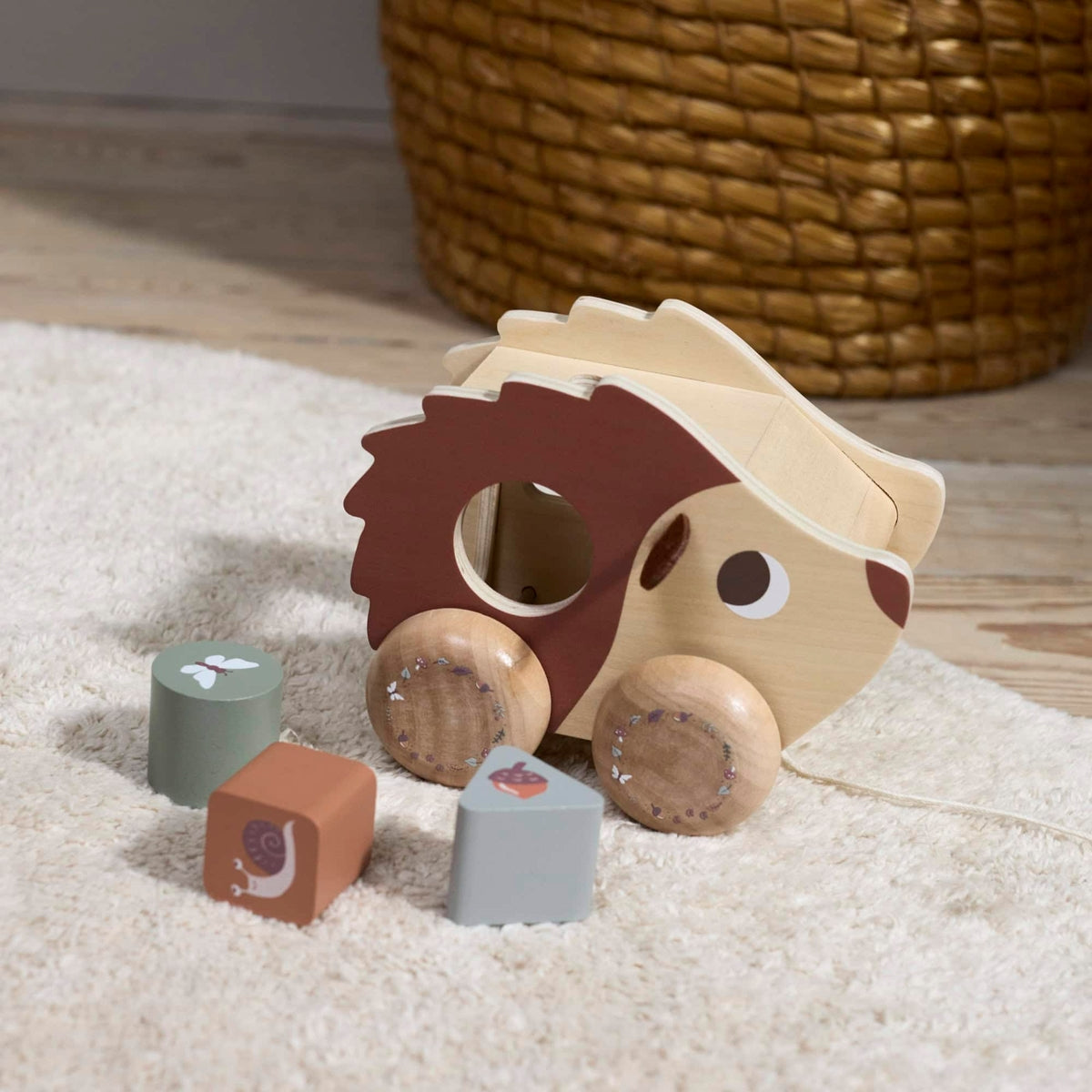 Houten vormenstoof op wielen in de vorm van een egel, met daarvoor gekleurde blokken met daarop illustraties van een vlinder, slak en eikel.