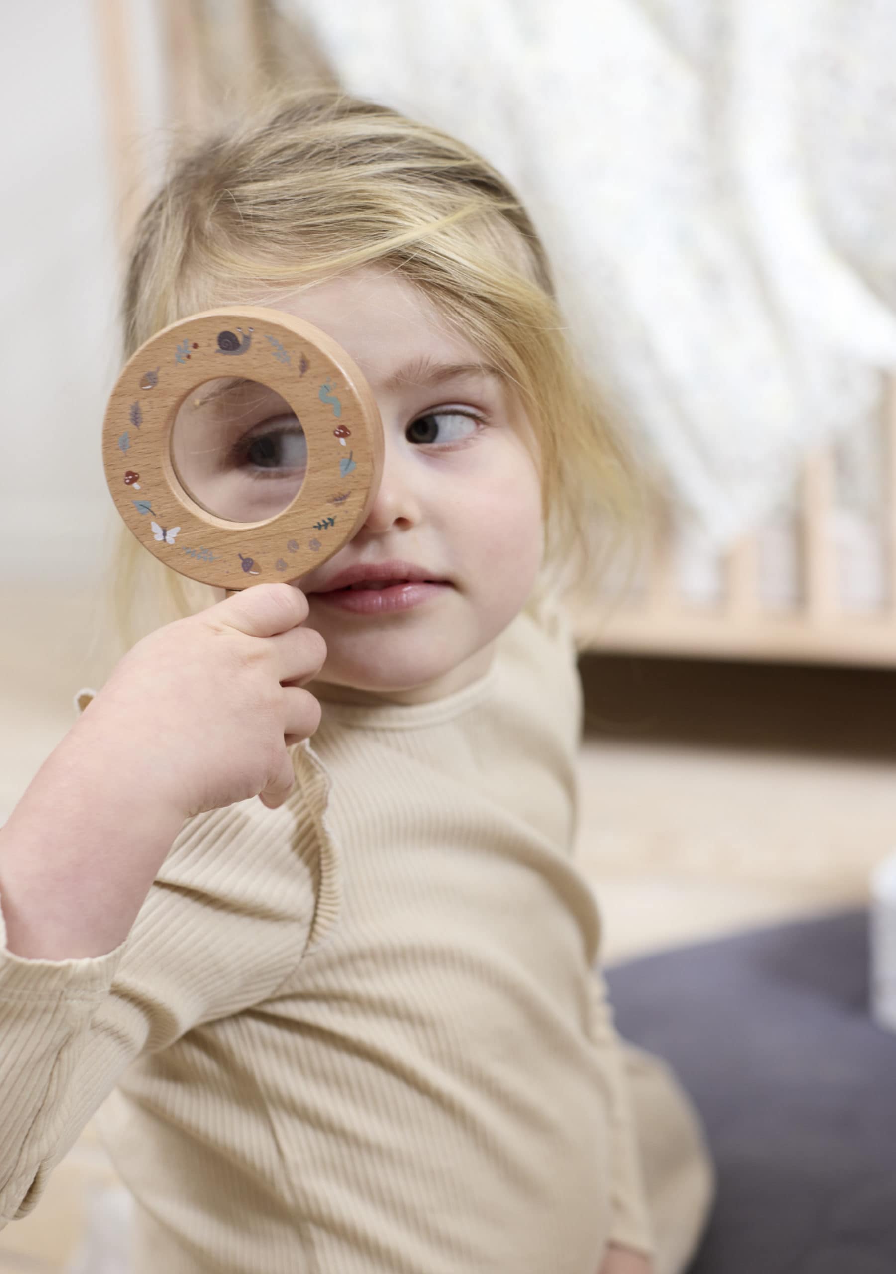 Meisje dat door het houten vergrootglas uit de ontdekkingsset van Filibabba kijkt.