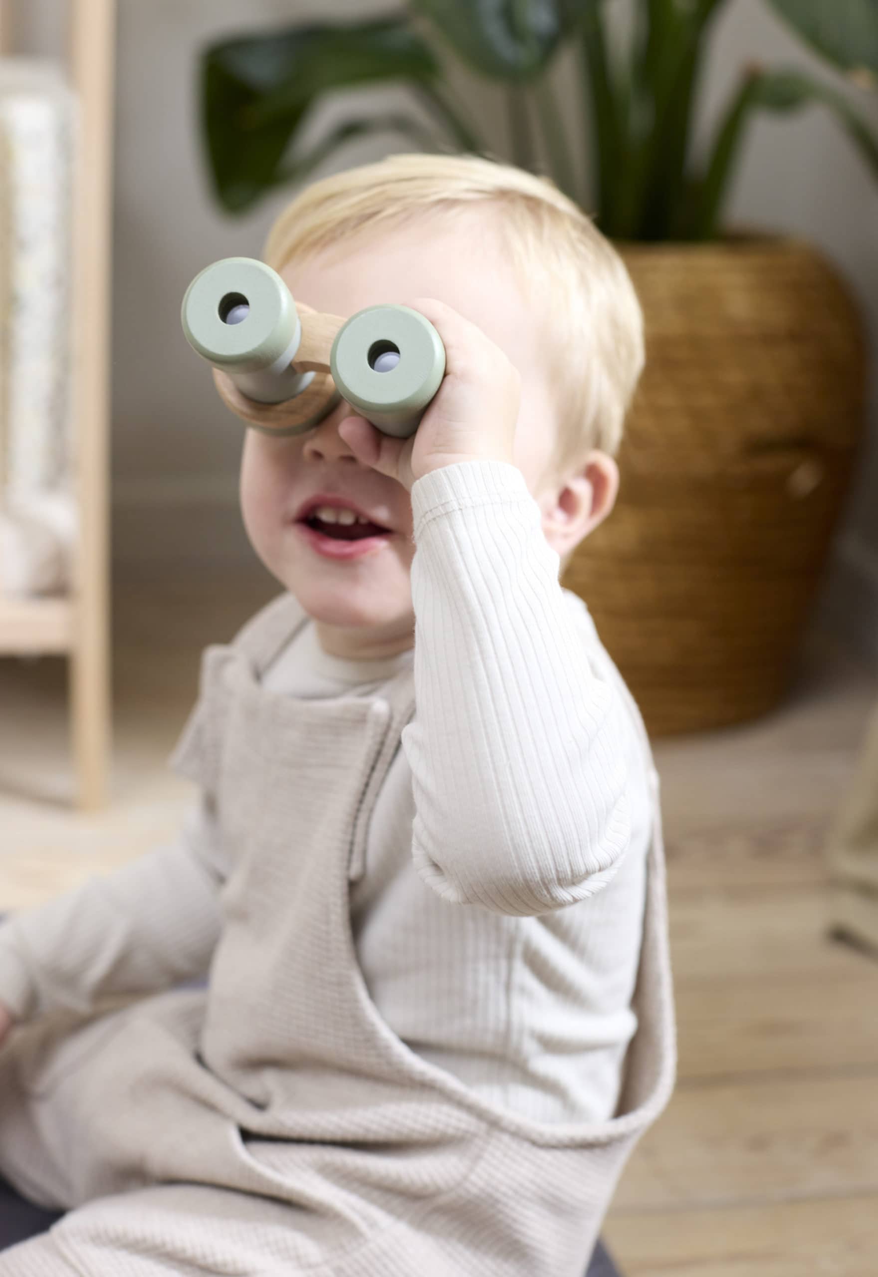 Een jongetje dat door de houten verrekijker uit de speelgoed ontdekkingsset van Filibabba kijkt.