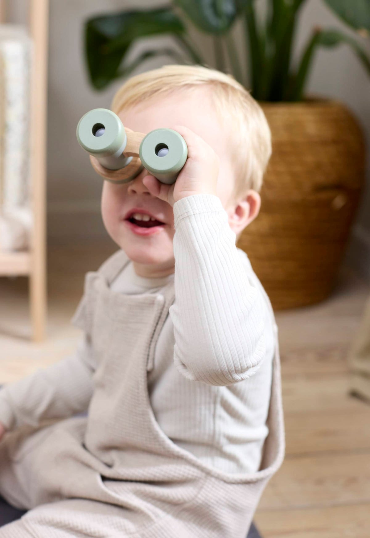 Een jongetje dat door de houten verrekijker uit de speelgoed ontdekkingsset van Filibabba kijkt.