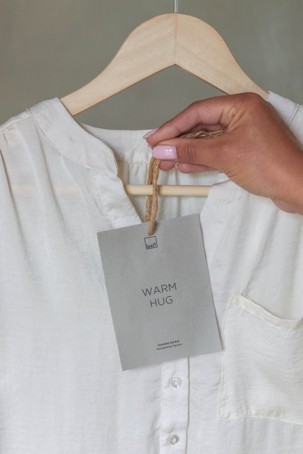 Foto van het geurzakje aan een blank houten hangertje bij een witte blouse