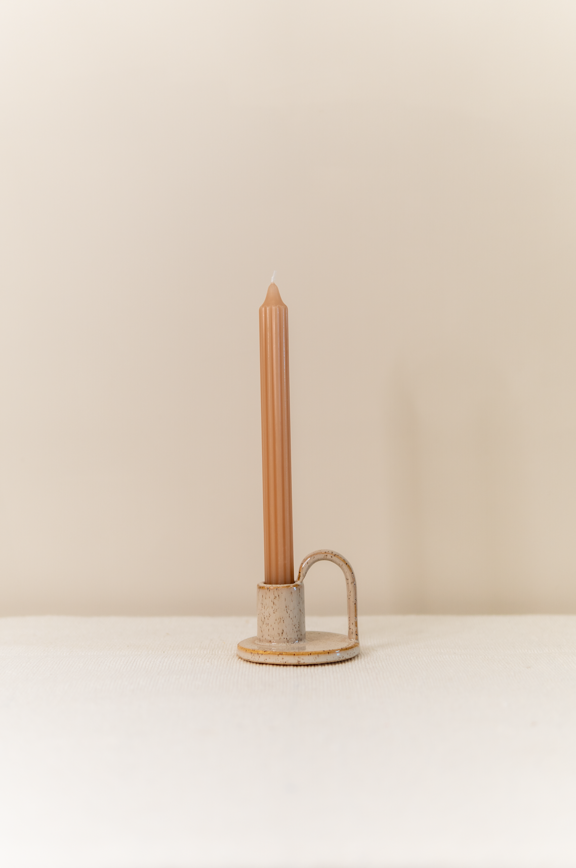 Een eenvoudige beige kandelaar van steen, met daarin een grooved dinerkaars, zowel de kaars als de kandelaar zijn van het merk Rustik Lys