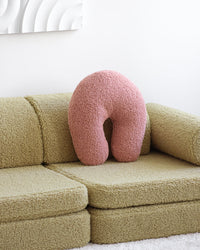 Het zachtroze Wigiwama sierkussen in guava pink springt eruit op een naturel groene teddy bank – een speelse combinatie die een moderne en gezellige sfeer creëert in de kinderkamer of woonkamer.