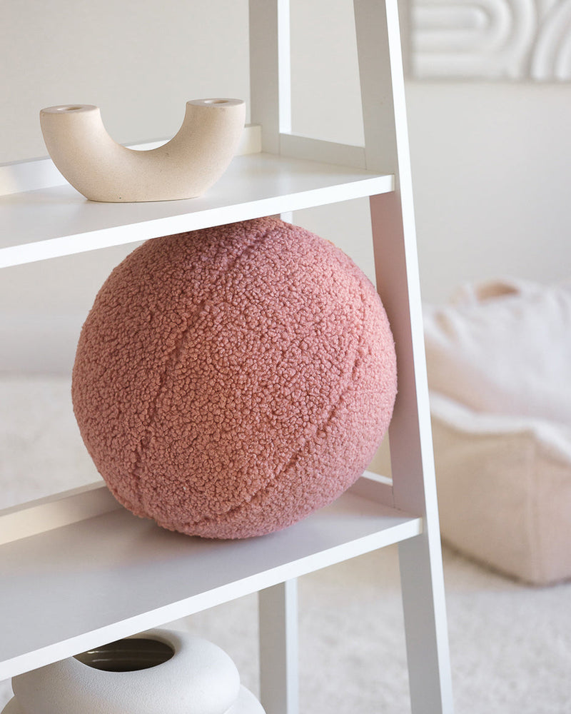 Het roze Wigiwama teddy sierkussen in guava pink als stijlvolle eyecatcher op een witte open kast. Ideaal als speels én decoratief element.