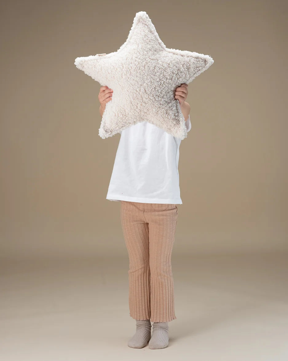 Kind houdt het stervormige teddy sierkussen van Wigiwama voor het gezicht – een speels en knus accessoire voor de kinderkamer.