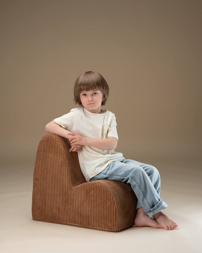 Kind zit op de Wigiwama Cloud loungestoel, zachte bruine ribstof fauteuil perfect voor ontspannen en lezen