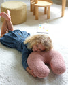 Een meisje ligt heerlijk op het zachte, ondersteunende sierkussen in guava pink – een kalme, zachtroze kleur die uitnodigt tot ontspannen, knuffelen en dagdromen. Ideaal voor elke kinderkamer.