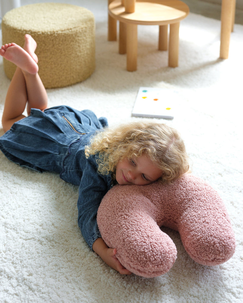 Een meisje ligt heerlijk op het zachte, ondersteunende sierkussen in guava pink – een kalme, zachtroze kleur die uitnodigt tot ontspannen, knuffelen en dagdromen. Ideaal voor elke kinderkamer.