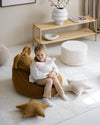 Een meisje zit op een zitzak en knuffelt het Wigiwama teddy kussen in biscuit – een zachte beige kleur – ideaal voor bed, speelhoek of fauteuil in een ruimte-thema kamer.