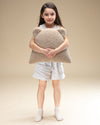 Een jong meisje houdt liefdevol een teddy sierkussen in de vorm van een beertje vast. Het zachte OEKO-TEX® teddystof in biscuitkleur maakt dit kussen een veilig en knuffelbaar accessoire voor de kinderkamer.
