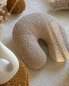Het biscuitkleurige teddy sierkussen ligt uitnodigend op een zacht vloerkleed – een decoratieve én functionele toevoeging aan elke speelhoek of leesplek in huis.