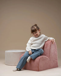 Meisje wat zit op een roze cloud stoel met daarnaast een witte ronde poef. Van het merk Wigiwama