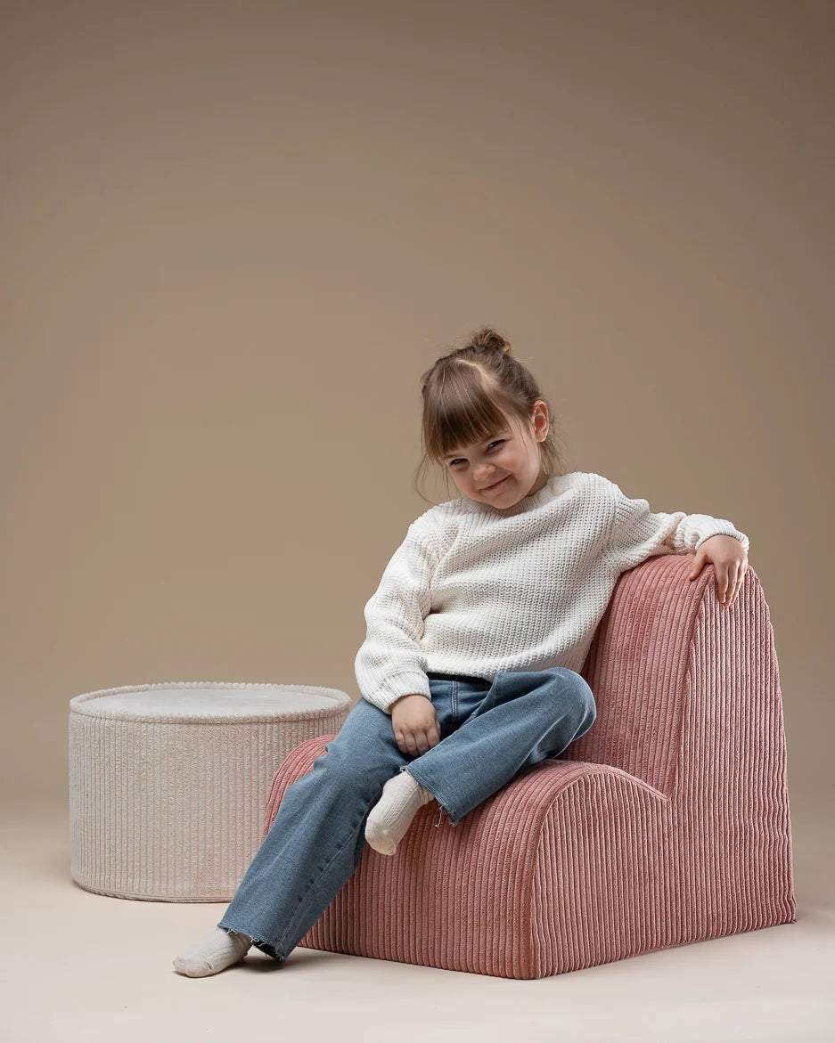 Meisje wat zit op een roze cloud stoel met daarnaast een witte ronde poef. Van het merk Wigiwama