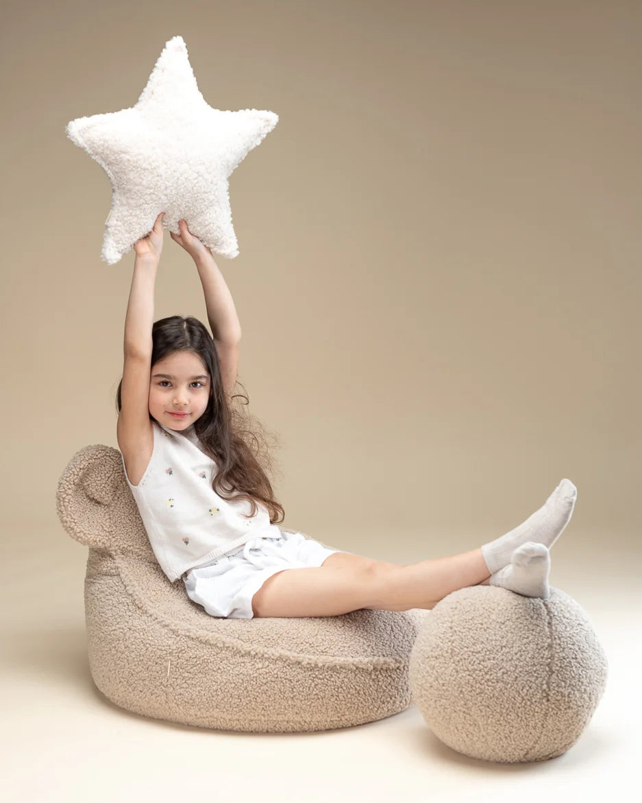 Meisje ontspant op een zachte teddy berenfauteuil met het stervormige sierkussen van Wigiwama – stijlvol en comfortabel.