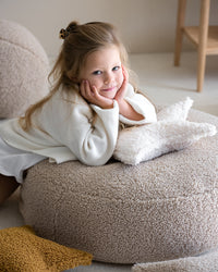 Meisje ligt op een beige teddy poef met het stervormige kussen van Wigiwama – perfect voor rustmomenten.