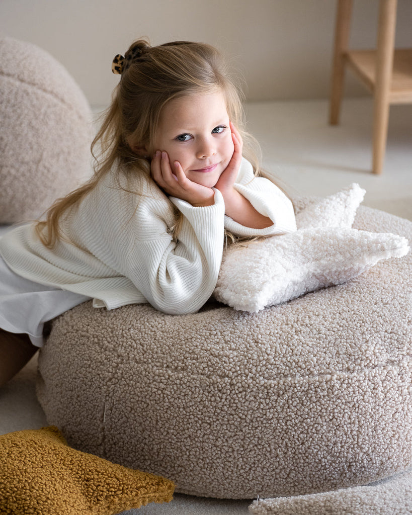 Meisje ligt op een beige teddy poef met het stervormige kussen van Wigiwama – perfect voor rustmomenten.