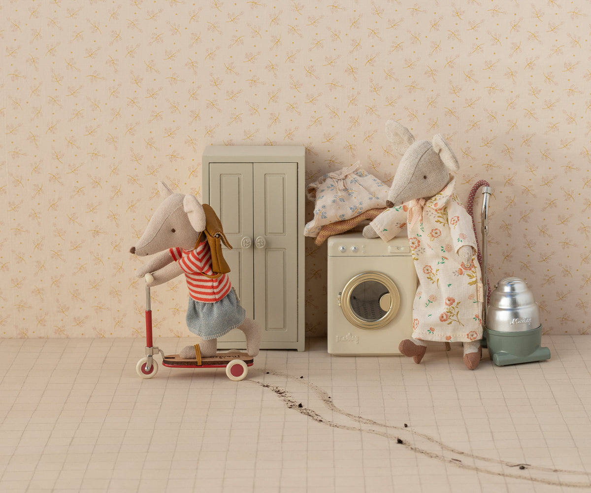Een Maileg muisje rijdt vrolijk rond op het rode metalen stepje, terwijl mama muis toekijkt in een sfeervol poppenhuisdecor met wasmachine en vintage stofzuiger. Deze speelse scène brengt het Maileg universum tot leven en laat zien hoe leuk en fantasierijk het miniatuur speelgoedaccessoire gebruikt kan worden in kinderkamers of als verzamelitem.