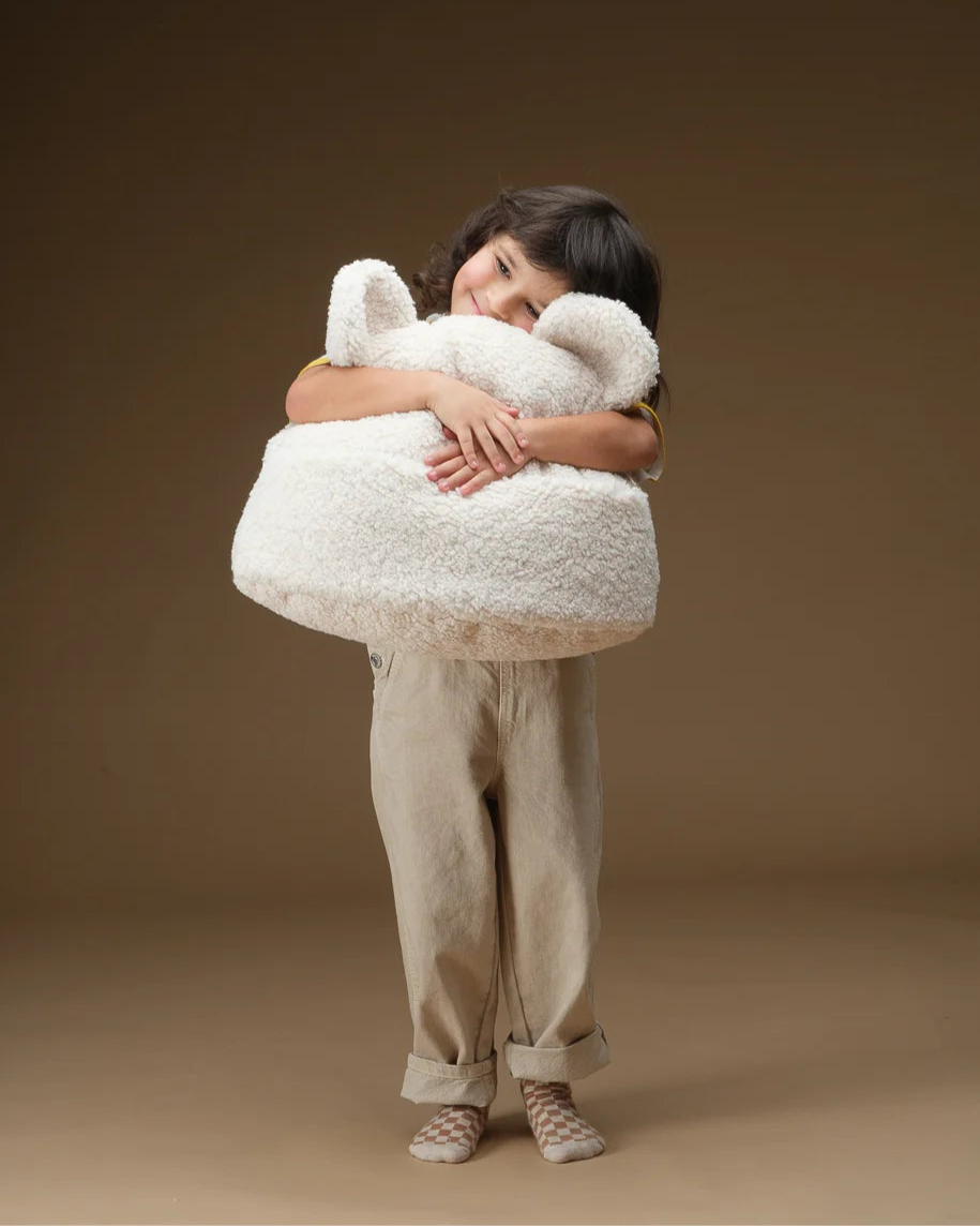  Een kind knuffelt het zachte Wigiwama beer kussen in cream – een aaibare, veilige keuze dankzij OEKO-TEX® gecertificeerde materialen en een heerlijk knuffelbare vorm (mét oortjes)