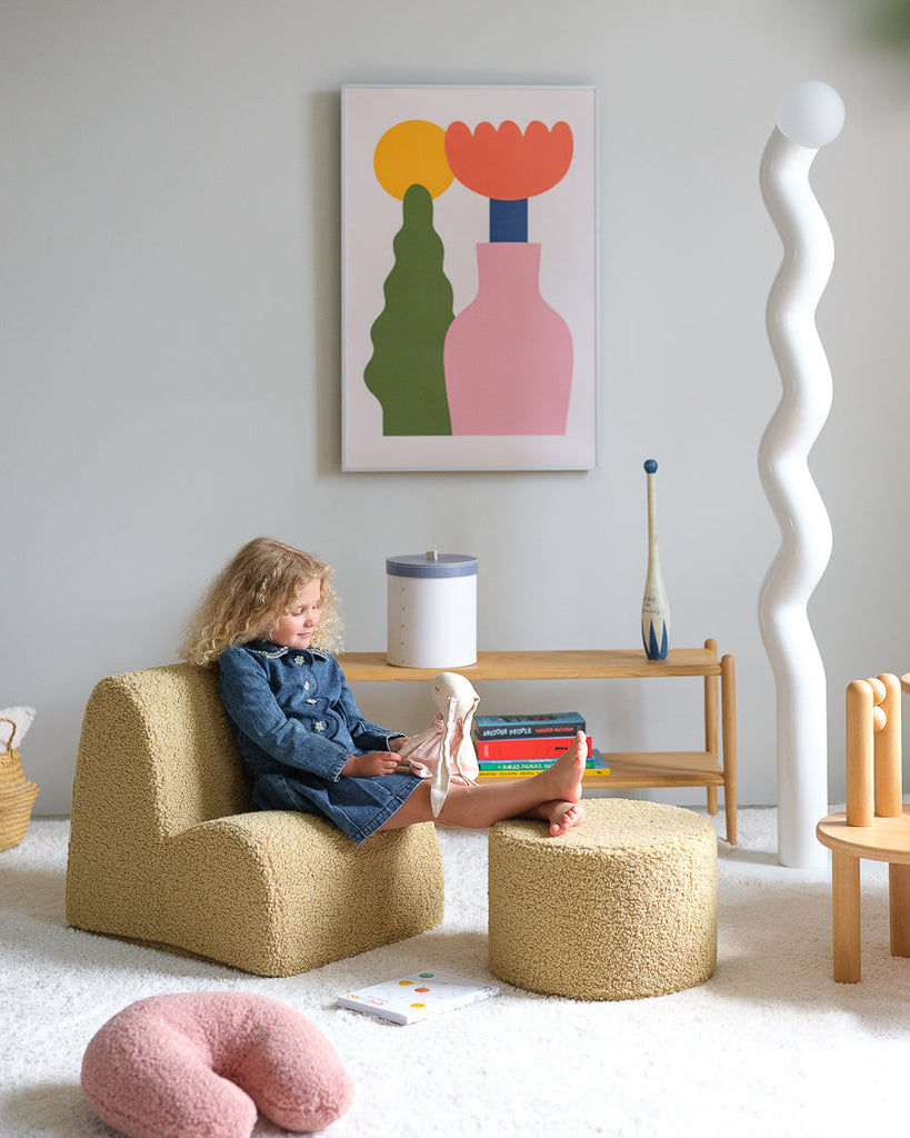 In een gezellige kinderspeelhoek zit een meisje ontspannen op een Wigiwama stoel met poef terwijl het U-vormige sierkussen in guava pink – een zachte, rustgevende roze tint – op haar wacht om mee te knuffelen of te loungen.