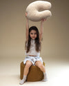 Een vrolijk meisje tilt het teddy sierkussen op in de lucht – het ideale accessoire voor knuffelmomenten, spelen of ontspannen lezen. De zachte stof en vriendelijke vorm zorgen voor comfort en veiligheid.