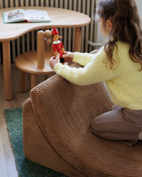 Meisje zit op de Wigiwama bruine stoel te spelen met een popje