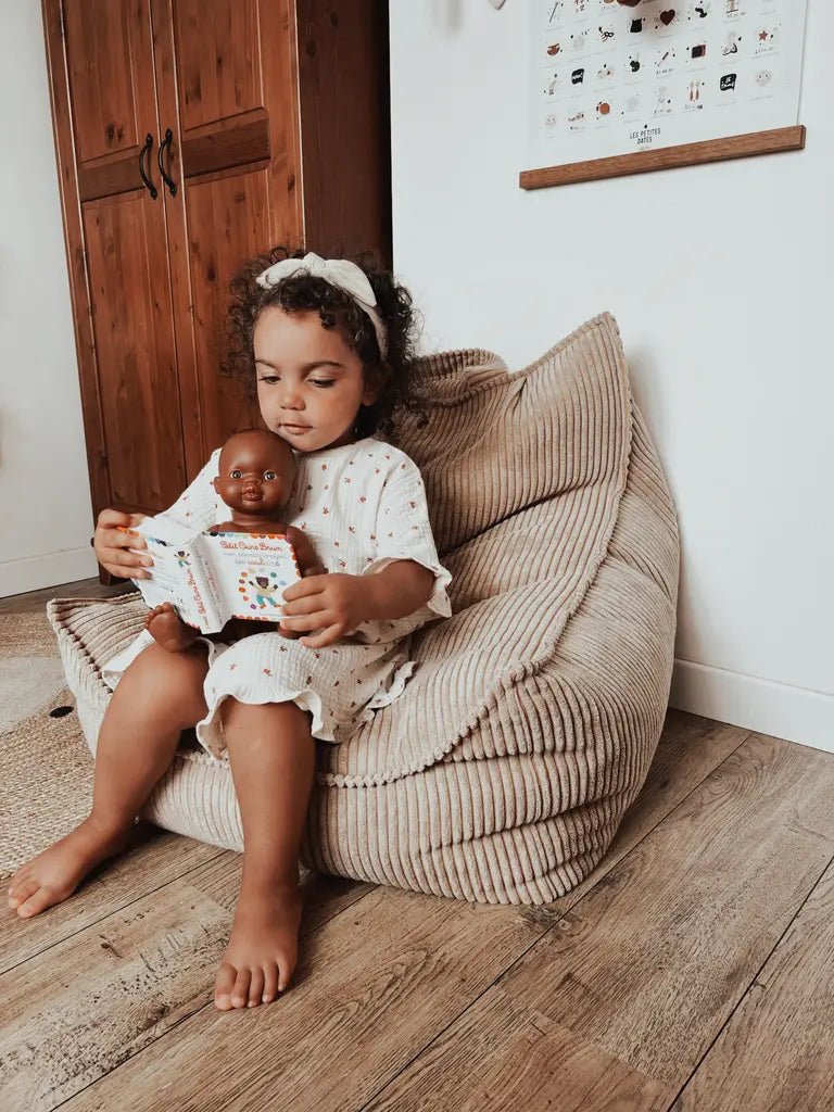 Meisje met donker haar speelt met pop terwijl ze comfortabel zit in de beige ribstof zitzak