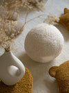 Het witte teddy bal kussen van Wigiwama als subtiel accent in een rustige slaapkamer. Gemaakt van OEKO-TEX® gecertificeerde stof voor een veilige en gezonde omgeving.