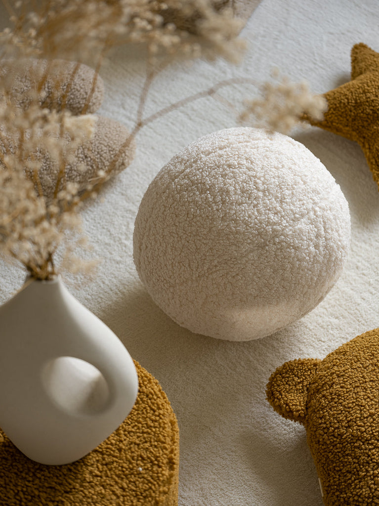 Het witte teddy bal kussen van Wigiwama als subtiel accent in een rustige slaapkamer. Gemaakt van OEKO-TEX® gecertificeerde stof voor een veilige en gezonde omgeving.