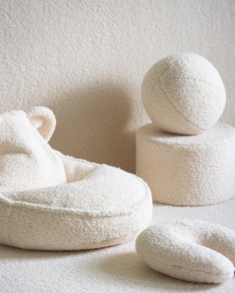 Sfeervol interieur in ton-sur-ton stijl, met het Wigiwama U-vorm kussen in cream wit als zacht en ondersteunend accent – perfect voor knusse leesmomentjes of ontspanning. Gecombineerd met een schattige zitzak met berenoortjes, een poef en een sierkussen in de vorm van een bal.