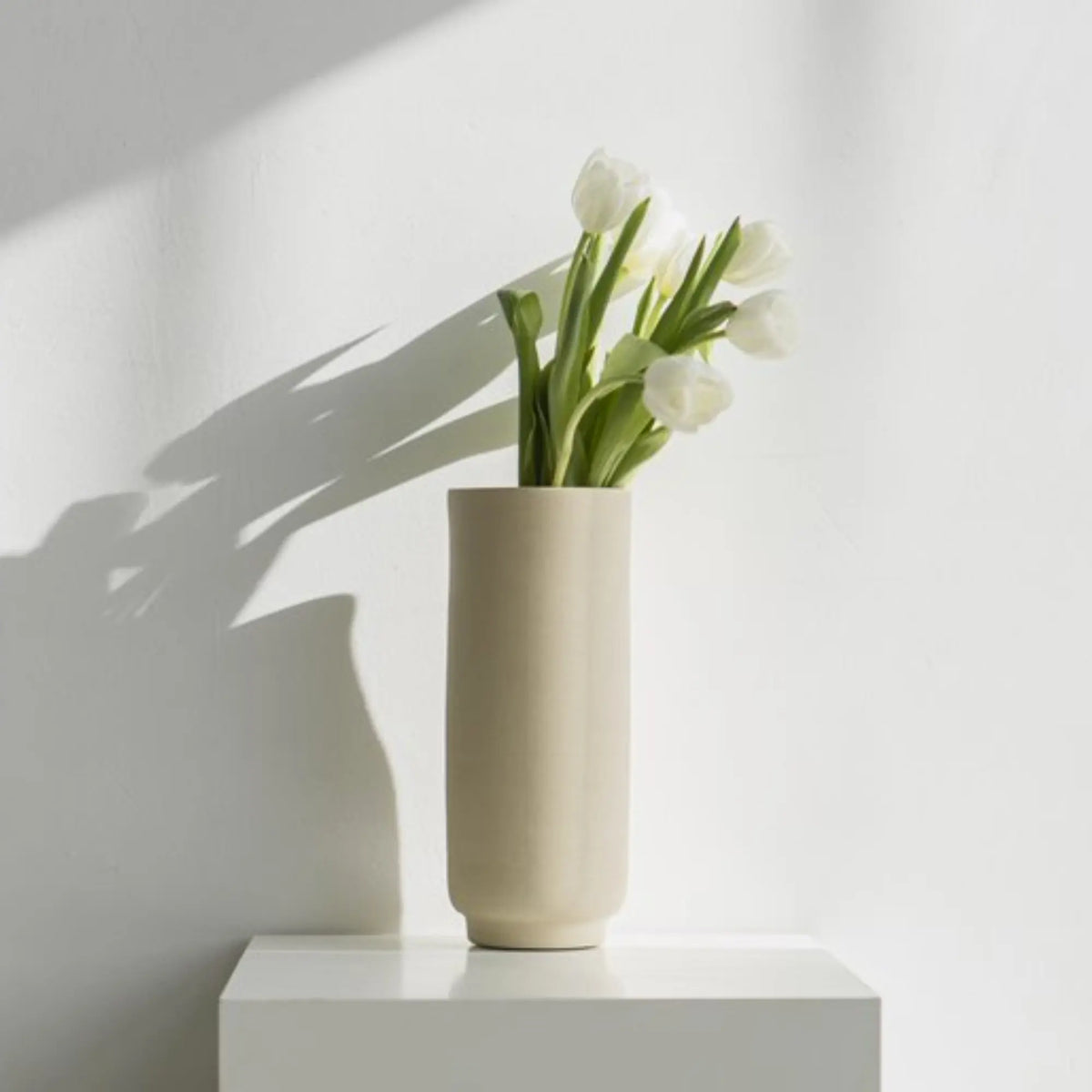 O Cactuu | Beige vaas Solvi met witte tulpen op een witte sokkel | Boetiek Blij