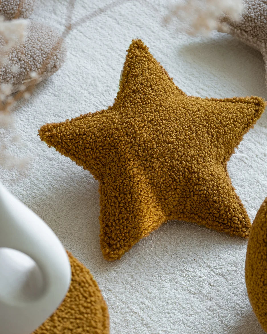 Het Wigiwama stervormige sierkussen in maple – een diepe okergele kleur – ligt als decoratief accent op een zacht vloerkleed in een rustige kinderkamer.