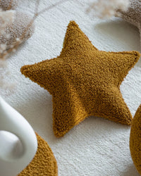 Het Wigiwama stervormige sierkussen in maple – een diepe okergele kleur – ligt als decoratief accent op een zacht vloerkleed in een rustige kinderkamer.