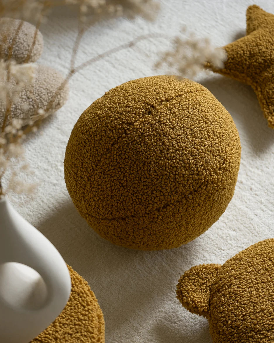 Close-up van het Wigiwama teddy sierkussen in maple kleur op een licht vloerkleed. Comfortabel, decoratief en gemaakt van veilige materialen voor kinderen.