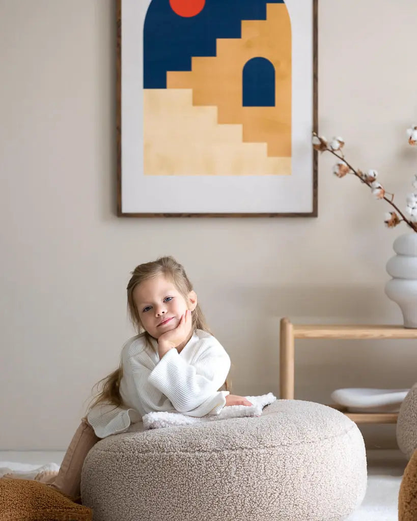 Sfeerbeeld van de ronde beige Wigiwama poef van zachte teddy stof, met daarop een lief meisje.