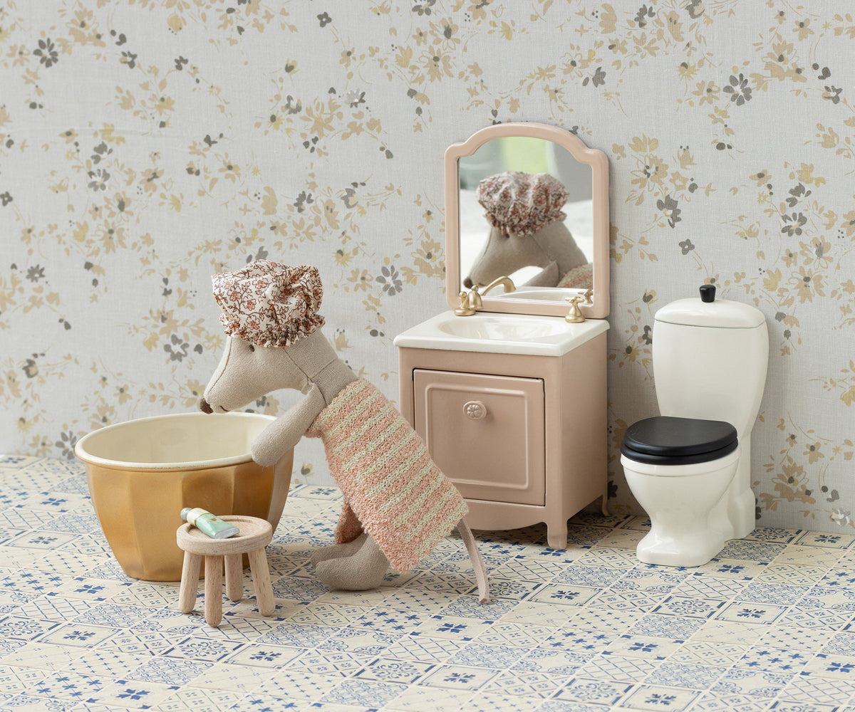 Sfeerbeeld van de Grote Zus die in de gouden badkuip tobbe wil stappen. In de badkamer ook een badmeubel met spiegel en een toilet.