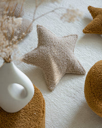 Het stervormige Wigiwama teddy kussen in biscuit – een neutrale beige tint – vormt een zacht accent op een licht kleed, ideaal voor een rustige, moderne kinderkamer.