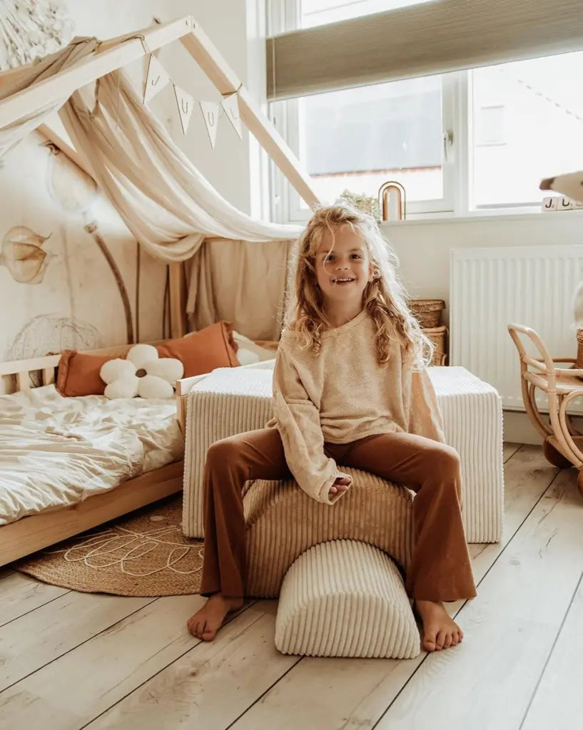 Meisje in een meidenkamer, ze zit op het grootste en beige blok van de regenboogvorm die hoort bij de 3-delige speelset.