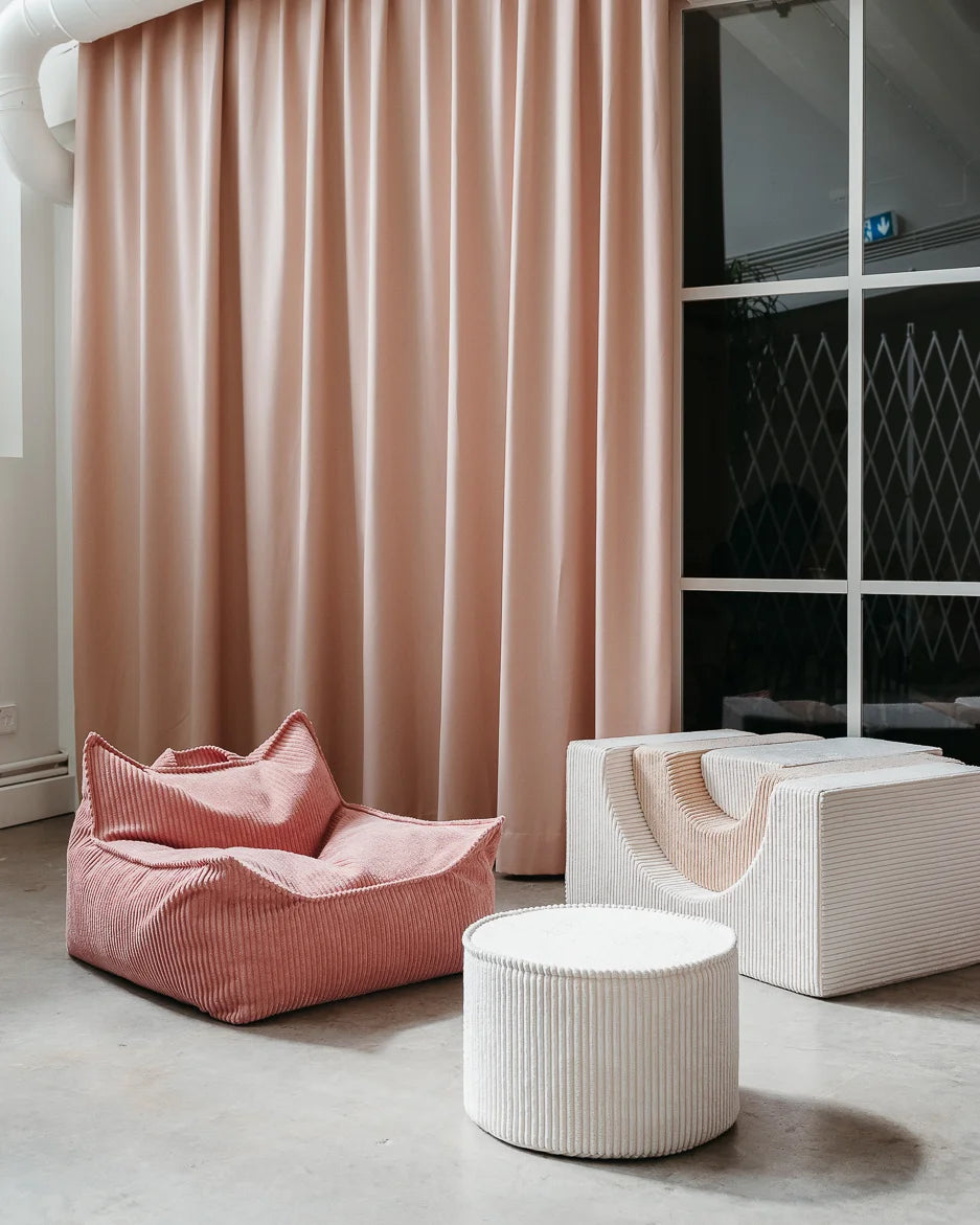 Een roze zitzak, een speelset en een marshmallow offwhite poef in een woonkamer met een roze gordijn. Een fijne plek voor je kindje om te zitten, chillen, hangen en spelen