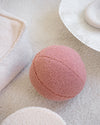 Guava pink teddy bal kinder sierkussen van Wigiwama op een licht tapijt. Gemaakt van OEKO-TEX® teddystof en perfect voor spelen, decoreren of relaxen.