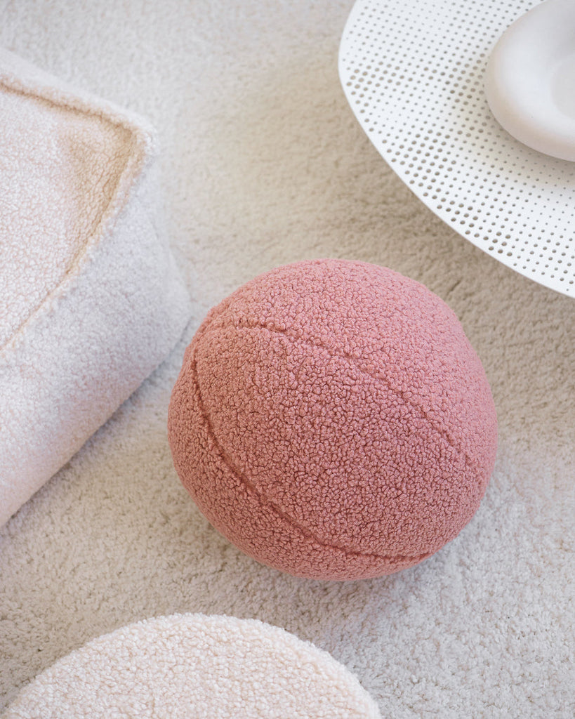 Guava pink teddy bal kinder sierkussen van Wigiwama op een licht tapijt. Gemaakt van OEKO-TEX® teddystof en perfect voor spelen, decoreren of relaxen.