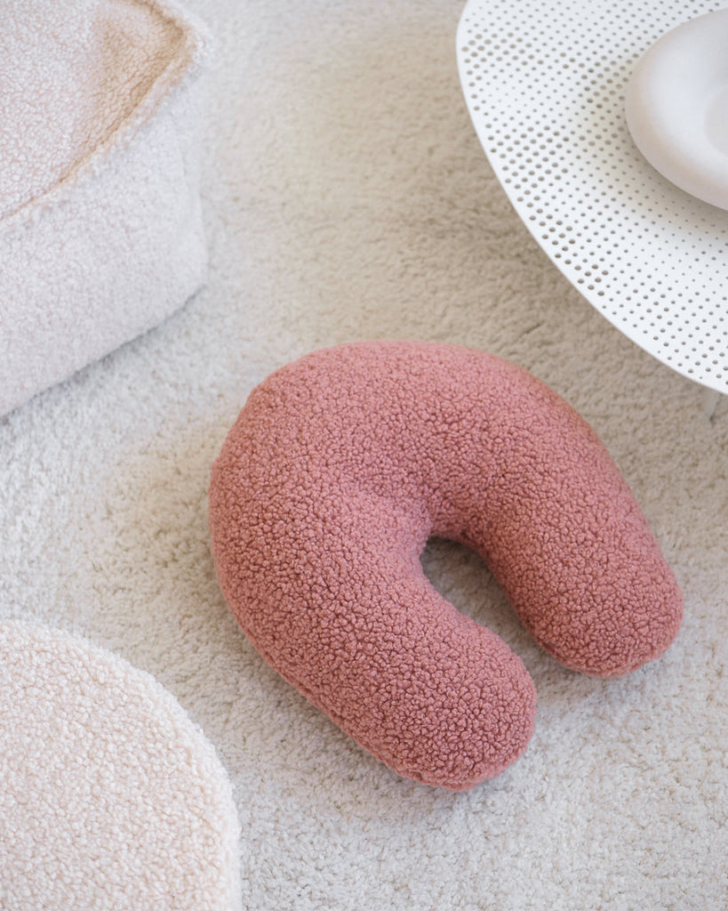 Het U-vormige kussen in guava pink – een serene zachtroze tint – ligt uitnodigend op een licht vloerkleed en voegt een speels én rustgevend accent toe aan de speelhoek, kinderkamer of woonkamer.
