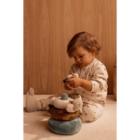 Een peuter in pyjama, spelend op de vloer, met de Beth Rabbit babyslofjes van LIEWOOD aan de voeten. Ze is aan het spelen met de Sannie Plush Stacking Tower.