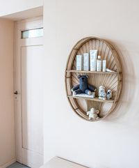 Sfeerbeeld van het ovale wandrek van KidsDepot, maar nu opgehangen aan de muur en gevuld met een knuffeltje, wat speelgoed en wat baby verzorgingsproducten.